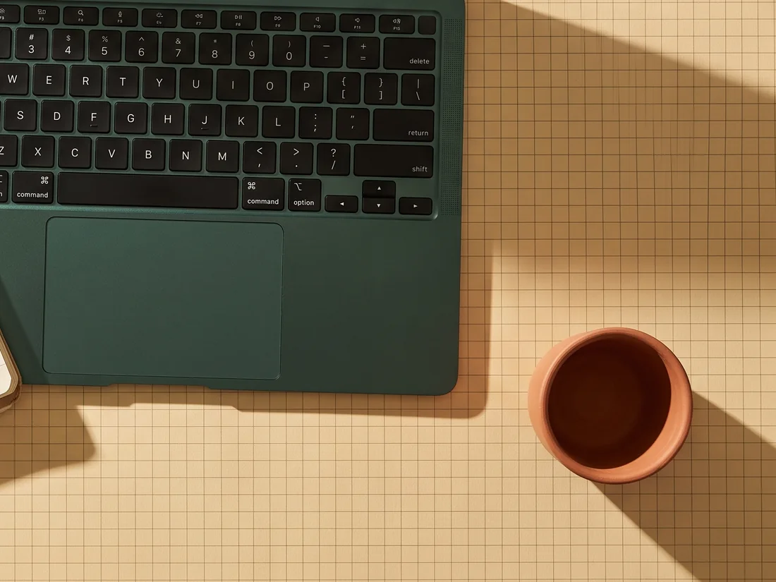 A laptop and a terracotta cup on squared paper, photographed from above, set up for an online tuition session