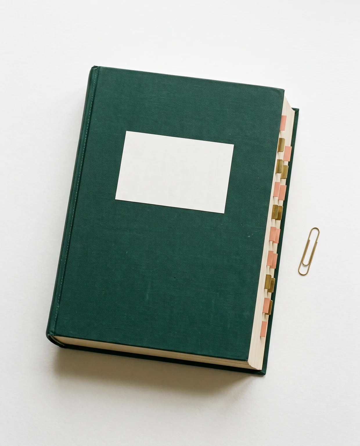 A bound dissertation in deep green cloth lying on a white surface, its pages marked with brass and terracotta tabs