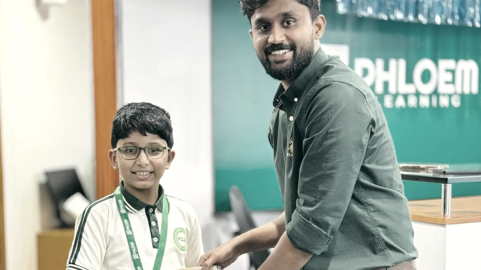 A tutor handing a student his work at the PHLOEM Learning reception in Abu Dhabi