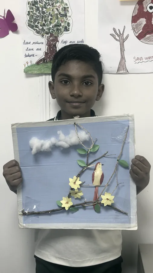 A student holding a framed picture of a bird made from twigs, cotton and paper