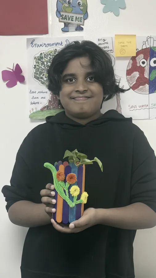 A student holding a flower vase built from lollipop sticks and paper flowers